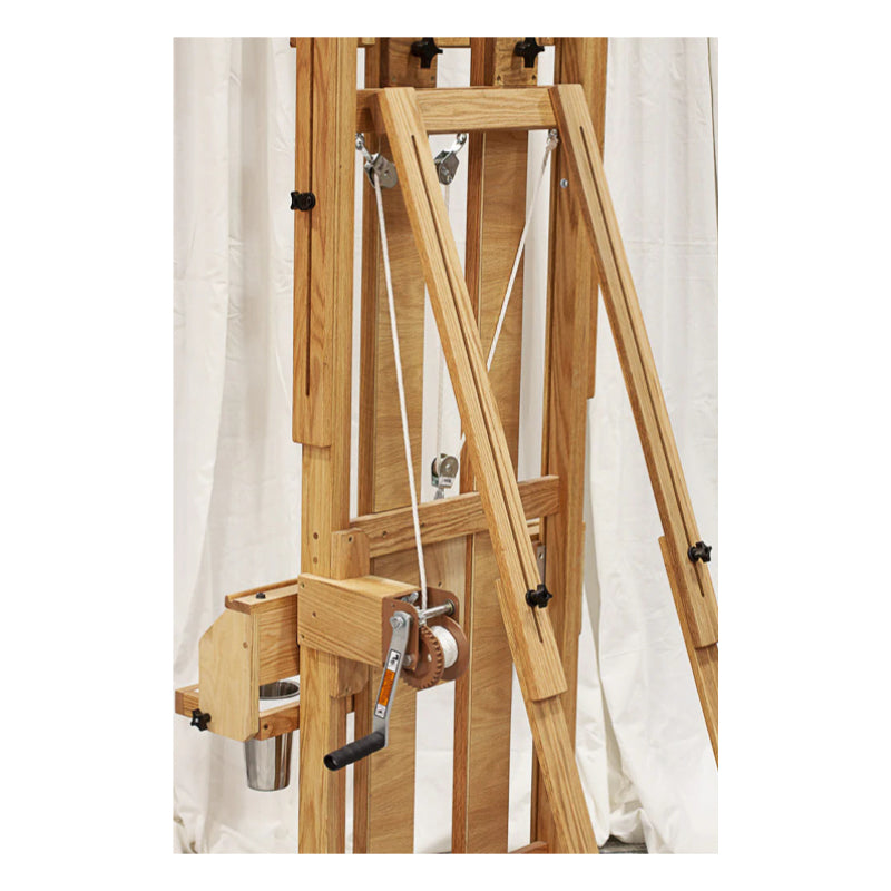 A BEST Classic Santa Fe II Easel by BEST with a marine style winch and white cords is set up against a white backdrop. The easel features adjustable supports and various knobs for customization of height and tilt.