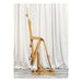 A side view of a BEST European Easel by BEST standing on a wooden floor with a white curtain backdrop. The adjustable easel, in a natural wood finish, is empty and extended in an upright position, ready to hold a canvas.