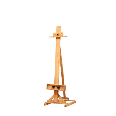A wooden BEST Chimayo easel stands on a plain white background. It has an adjustable center support and an artist utility shelf for holding art supplies or a canvas. The structure is clean and simple, made predominantly of light-colored wood.
